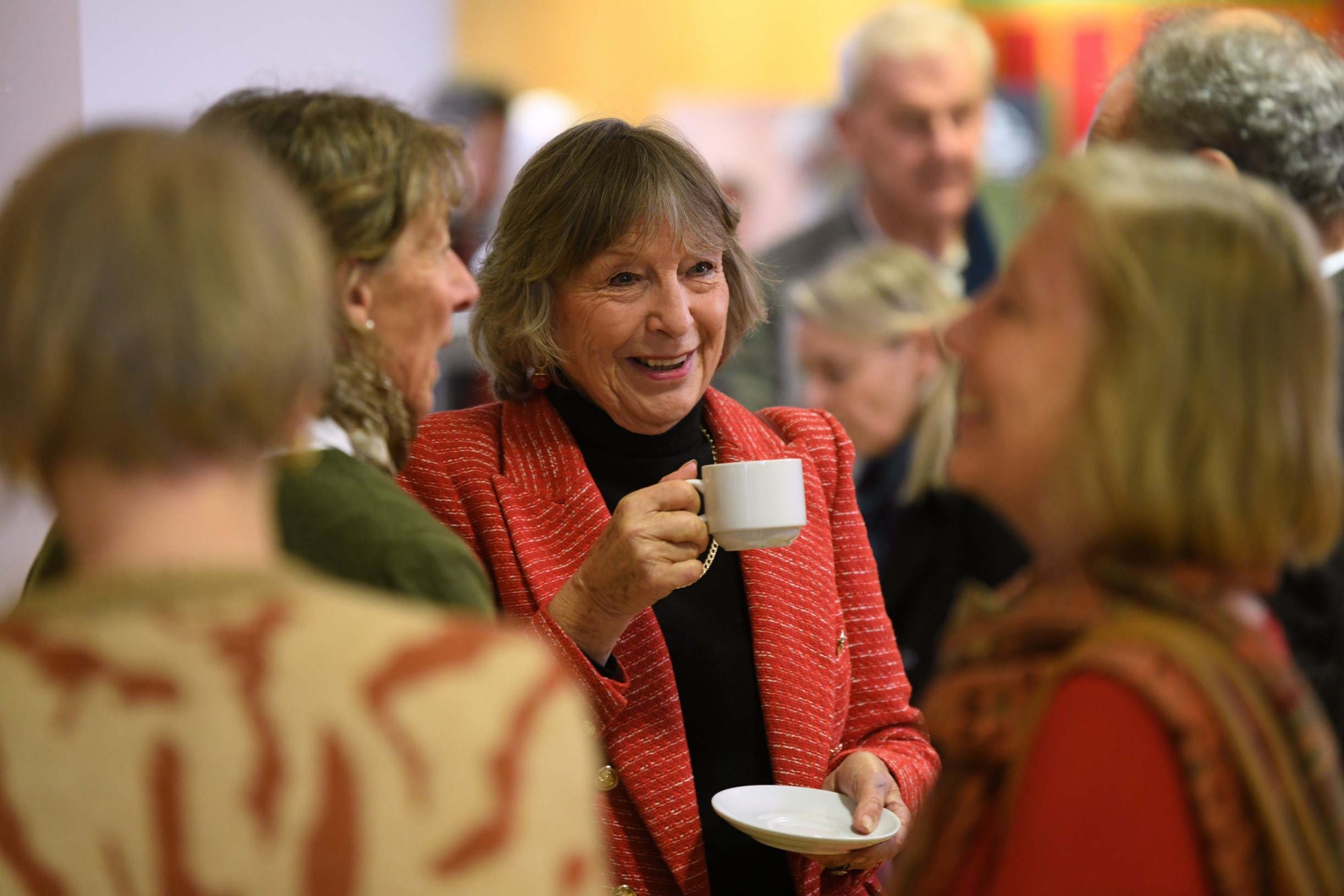 A woman with a cup of tea smiling in conversation