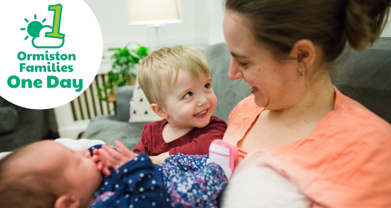 A mother holds a baby and toddler, who is smiling at her