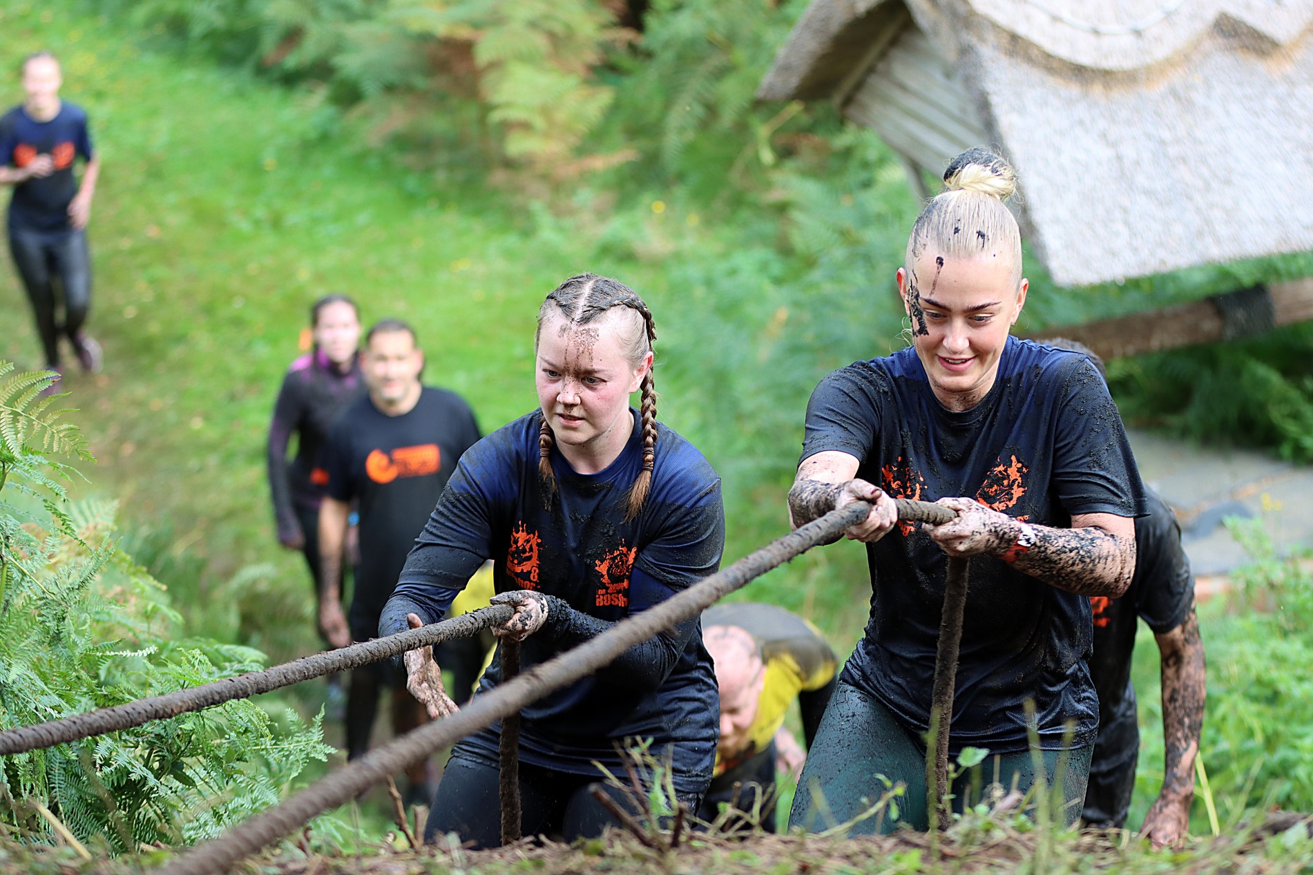 Two women climb up a hill using a rope at the Whole Hog muddy obstacle course